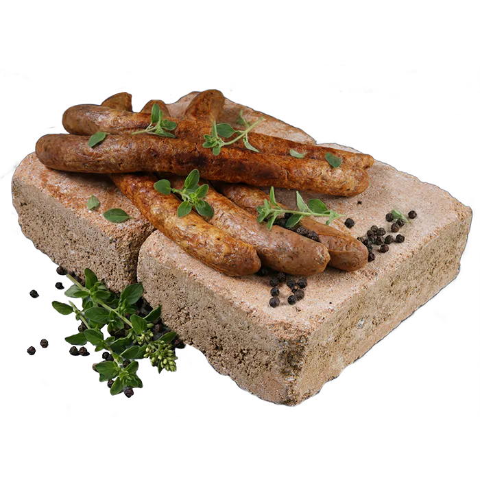 Vier gegrillte vegane Bratwürste auf einem braunen Backstein, garniert mit frischem Oregano und schwarzen Pfefferkörnern, auf weißem Hintergrund.